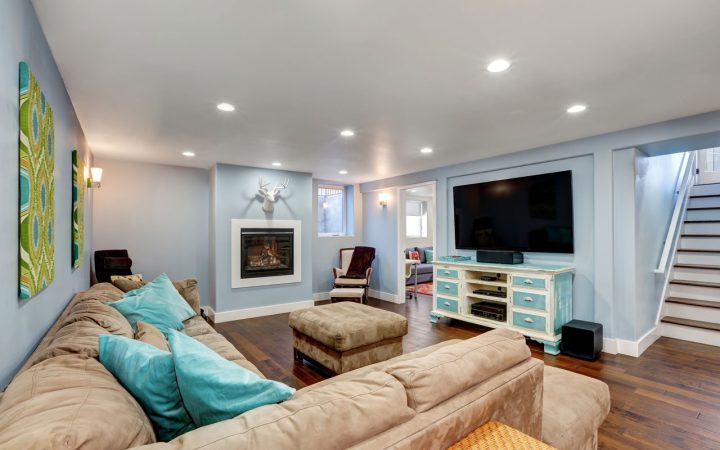 Comfortable finished basement family room featuring blue walls, hardwood floors, a beige sectional sofa, fireplace, large television, and bright recessed ceiling lights.