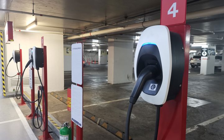 Multiple red and white electric vehicle charging stations installed in numbered parking spots within a well-lit indoor parking garage.