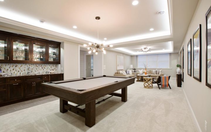 High-end finished basement featuring a pool table, wet bar with dark wood cabinetry, modern sputnik chandelier, recessed ceiling lights, and comfortable seating area with elegant layered lighting design